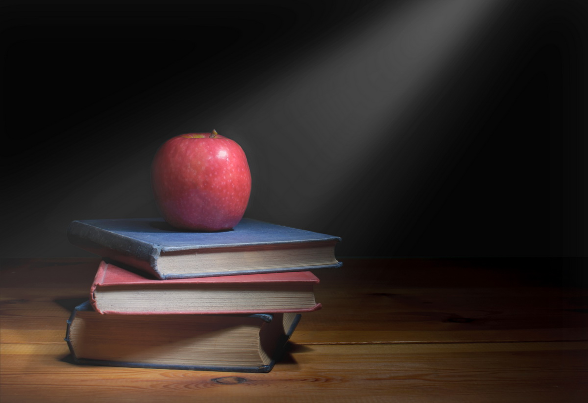 Ray of light shining down on a stack of books with a red apple