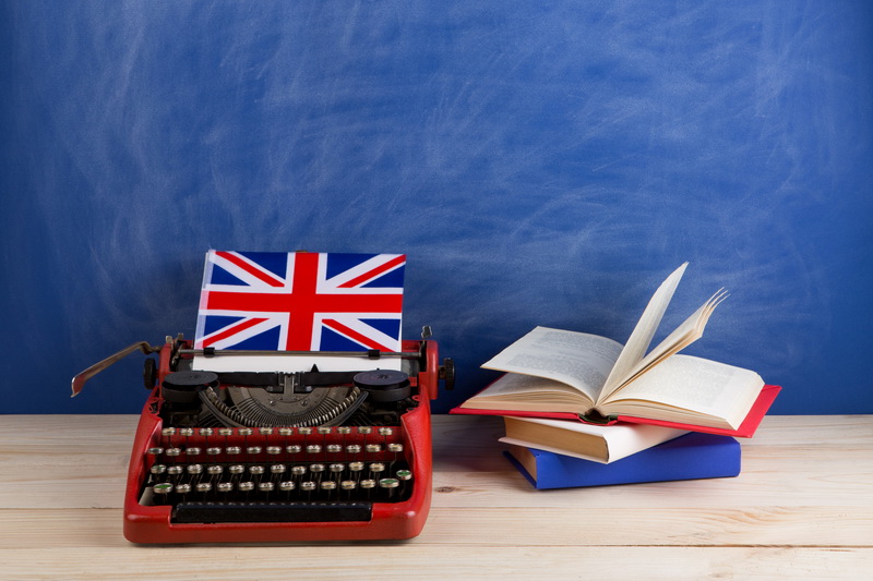 Political, news and education concept - red typewriter, flag of the United Kingdom, books on table against the background of the blue school board