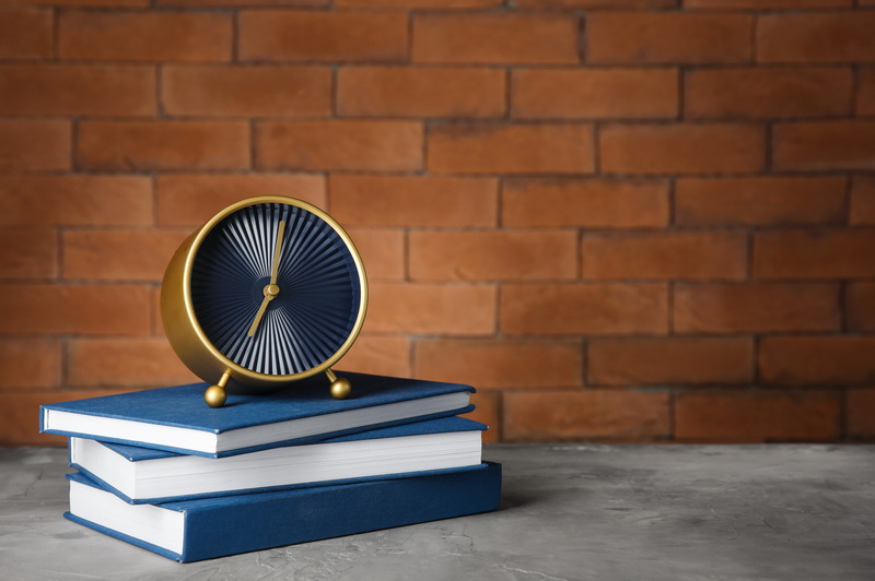 Alarm clock with books on table against brick background. Time management concept
